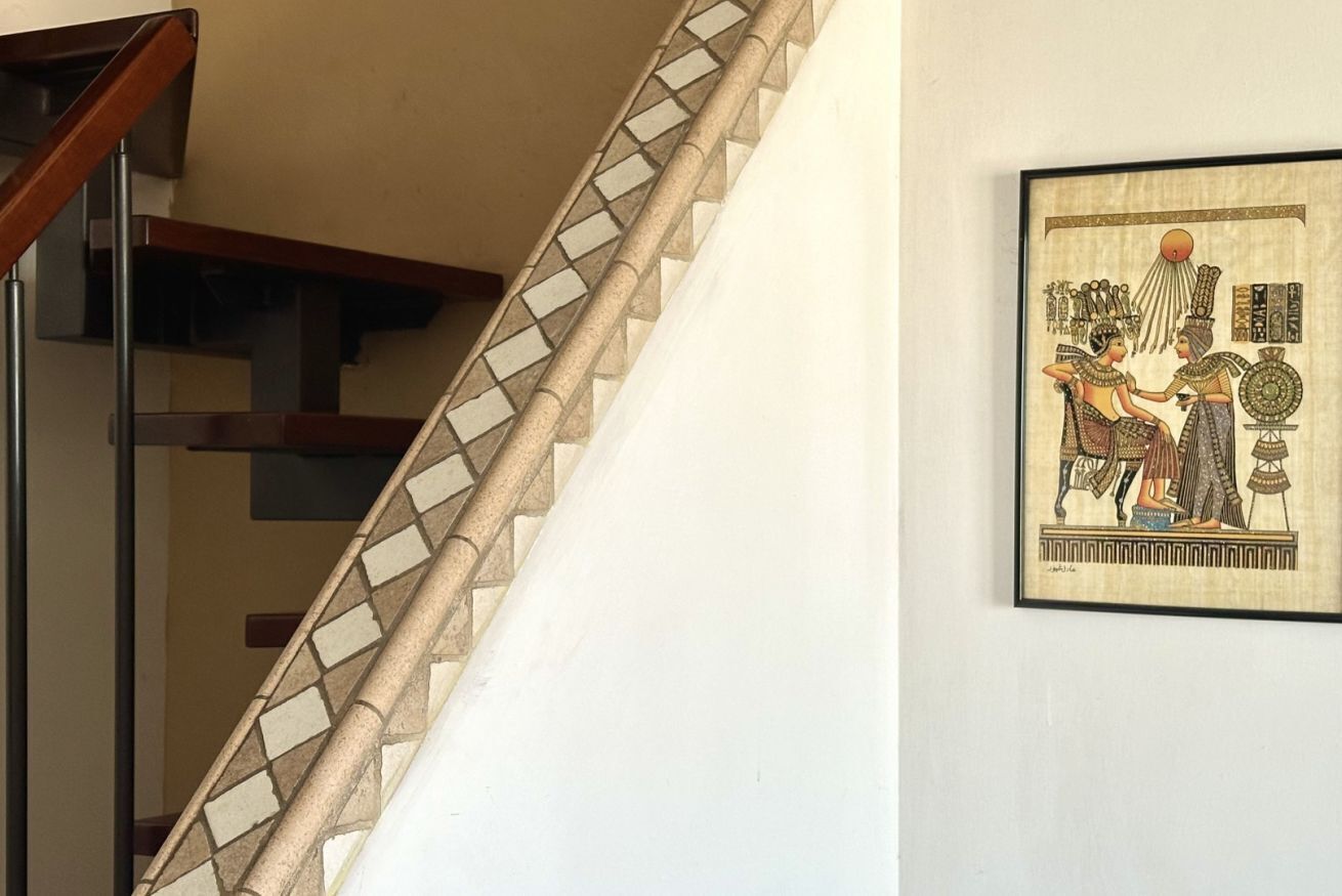 A staircase with a geometric tile pattern, a framed ancient Egyptian artwork on the wall, and a modern wooden handrail.