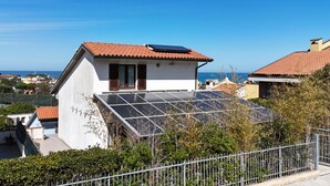 Et hus med solpanel på taget, omgivet af grønt og en klar himmel.