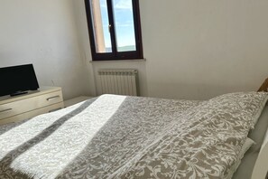 Een slaapkamer met een bed, een dressoir, een radiator en een raam.