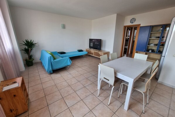 Een kamer met een eettafel, stoelen, een bank, een televisie en een kast.