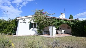 Edifici blanc amb teulada de rajola, una petita torre i una zona d'estar exterior coberta amb cadires blanques.