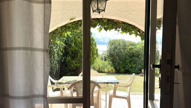 Una porta oberta que dona a un pati exterior amb taula i cadires, vistes a verdura i una làmpada.