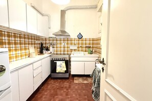 A compact kitchen with white cabinets, a stove, a sink, and a tiled backsplash.