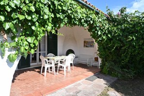 Een terras met een tafel en stoelen, een witte muur en een groene structuur begroeid met klimop.