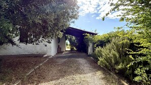 Un camí que condueix a un edifici amb reixa, envoltat de vegetació i un cel clar.