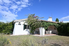 A white building with a tiled roof, a small tower, and a covered outdoor seating area with white chairs.