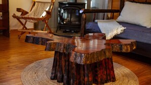 Una mesa de madera rústica con un diseño singular, un sofá azul con un cojín blanco, y una alfombra tejida sobre un piso de madera.