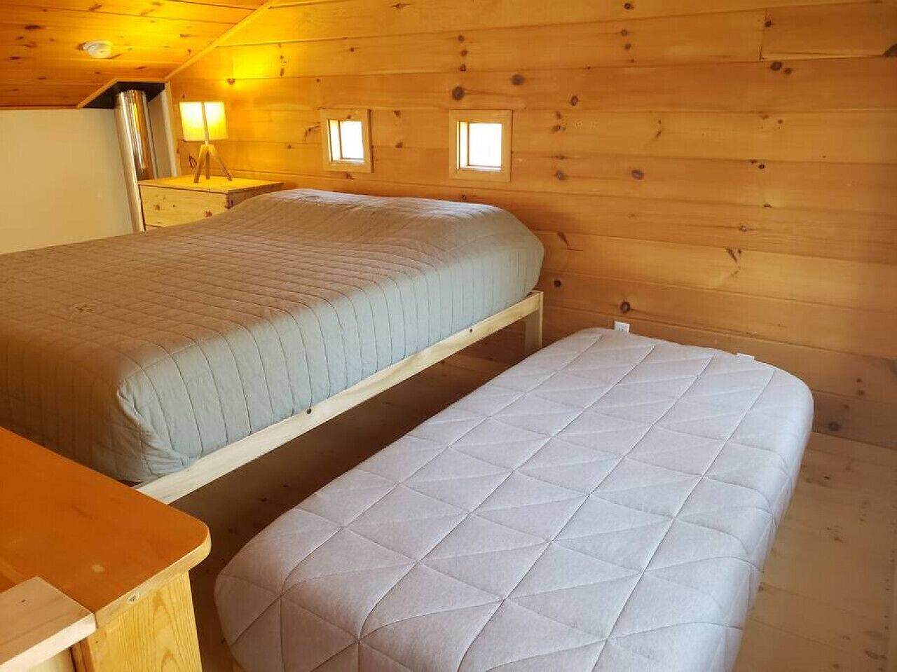 A cabin with two beds, a wooden table, and a small desk with a lamp.