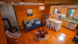 Un acogedor interior de cabaña con suelo de madera, un sofá, una mesa de comedor y una zona de cocina.