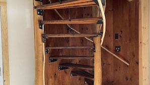 Eine Wendeltreppe mit Holzstufen und Metallgeländern in einem Raum mit Holzwänden und Fliesenboden.
