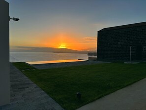 Vista do pôr do sol a partir de um edifício com parede de tijolos e área gramada na frente.