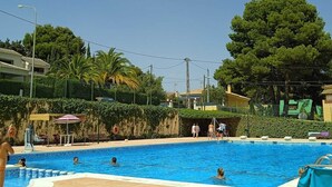 A swimming pool area with a tiled deck, lounge chairs, and a large tree in the background. - Do you need to take a break between mountains in a charming village in Alicante? (La Torre de les Maçanes)