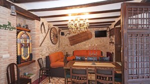 A rustic room with exposed beams, a chandelier, a wooden table, and a television mounted on the wall. - Do you need to take a break between mountains in a charming village in Alicante? (La Torre de les Maçanes)