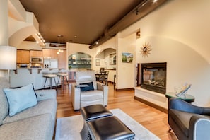 Cozy living space with a comfortable seating area, fireplace, and kitchen in the background.