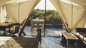 Un hébergement sous tente comprenant une table et des chaises en bois, un canapé et une vue sur la verdure environnante.