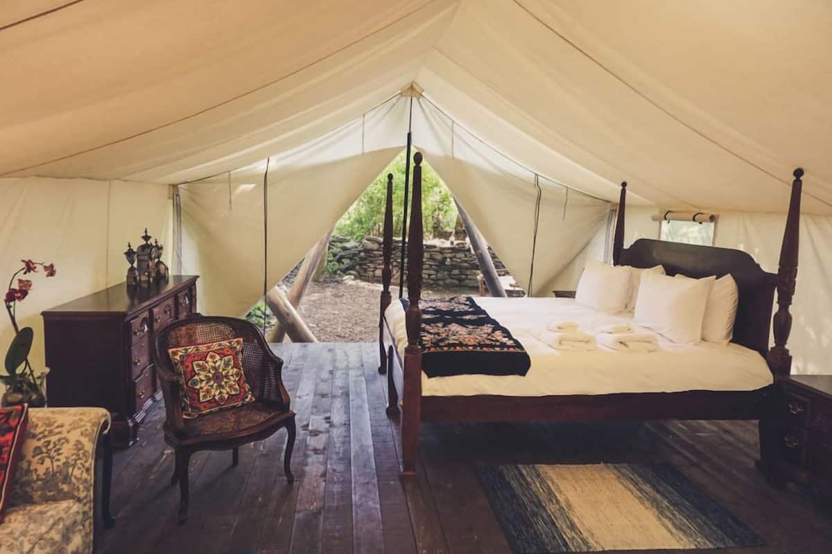 A tented room with a four-poster bed, a wooden chair, a small table, and a dresser.