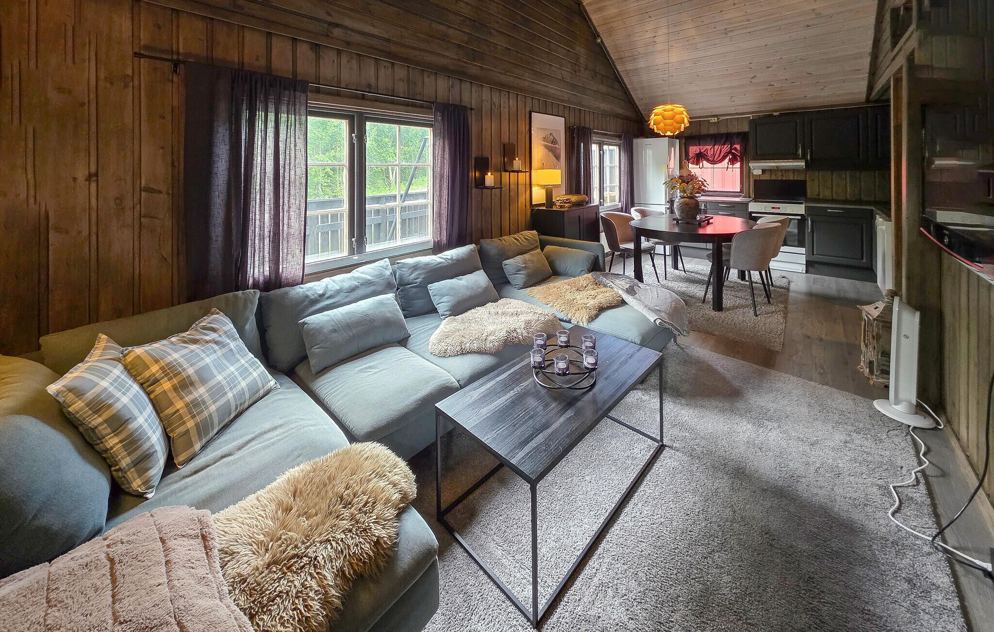 A cozy cabin interior with a sofa, a coffee table, a dining table, and a kitchen area.