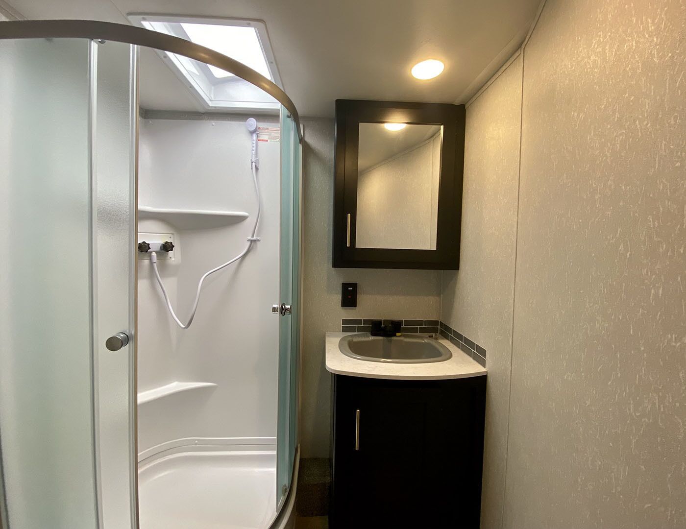 A bathroom with a glass-enclosed shower, a sink, and a mirror above it.