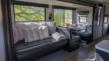 A cozy interior with a leather sofa, a small table with a bowl and glasses, and a window with a view of trees.