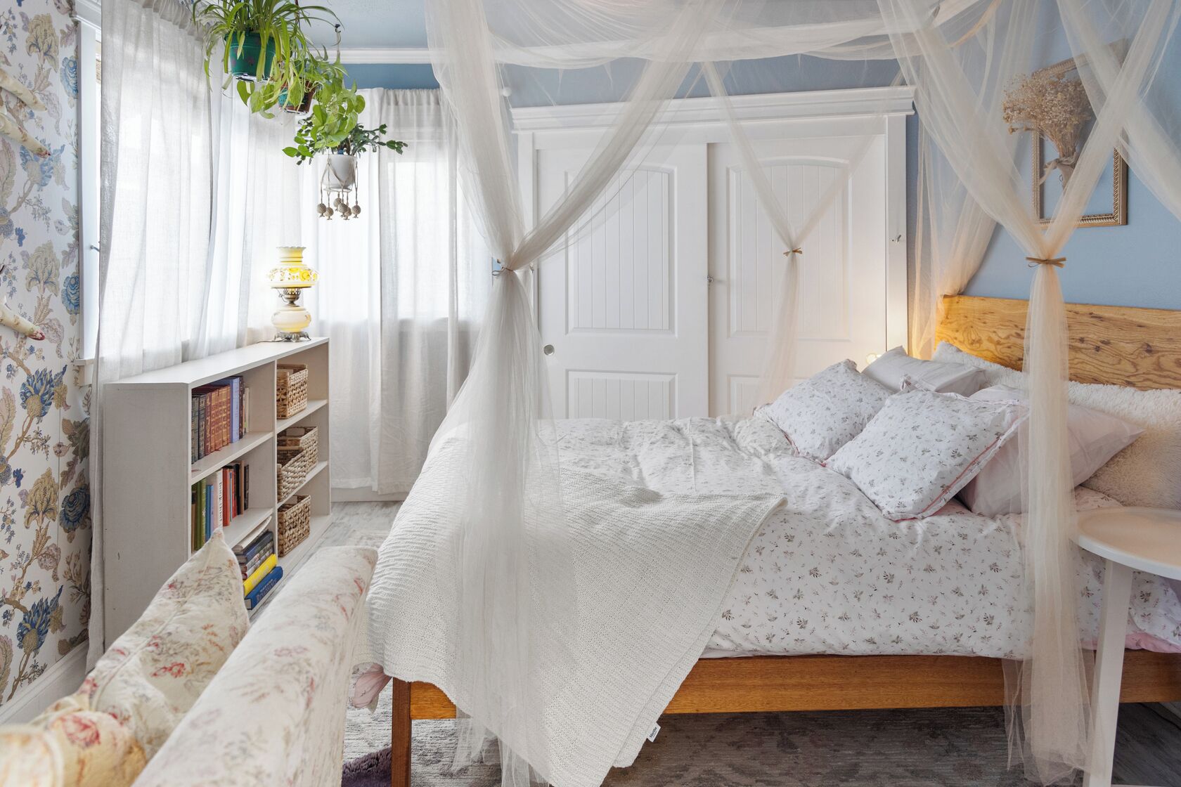 Un dormitorio con cama a dosel, una mesita de noche, una estantería y una ventana con cortinas.