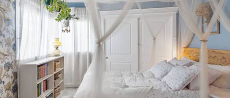 Un dormitorio con cama a dosel, una mesita de noche, una estantería y una ventana con cortinas.