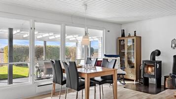 Une salle à manger moderne avec une grande table, des chaises et une vue sur l’extérieur.