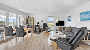 Een moderne woonkamer met een open haard, een eethoek met stoelen en een tafel, een bank en een televisie.