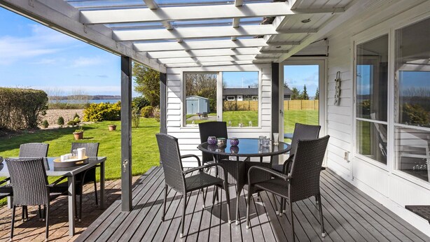 Een overdekt terras met een tafel en stoelen, uitkijkend op een gazon en een weids uitzicht.