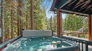 Un jacuzzi con cubierta de madera y una hamaca, rodeado de árboles altos.