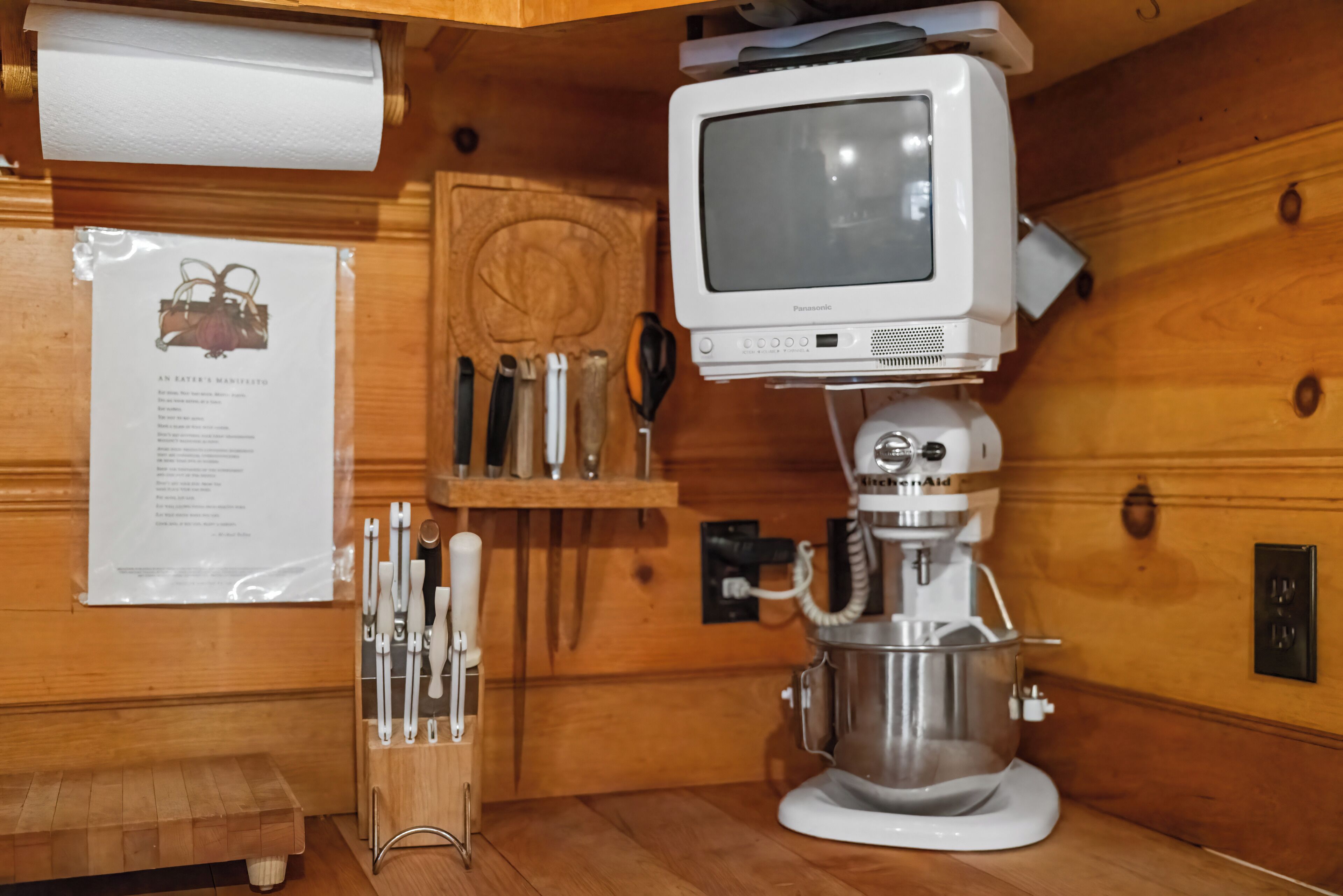 A kitchen with wooden paneling, a Panasonic TV mounted above a KitchenAid mixer, and a knife block on the counter.