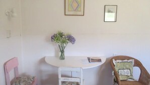 A room with a white table, two chairs, a vase with flowers, and two framed pictures on the wall. - Walnut Whare (Te Whiti)