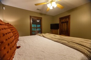 A bedroom with a bed, a ceiling fan, a television, and wooden doors.