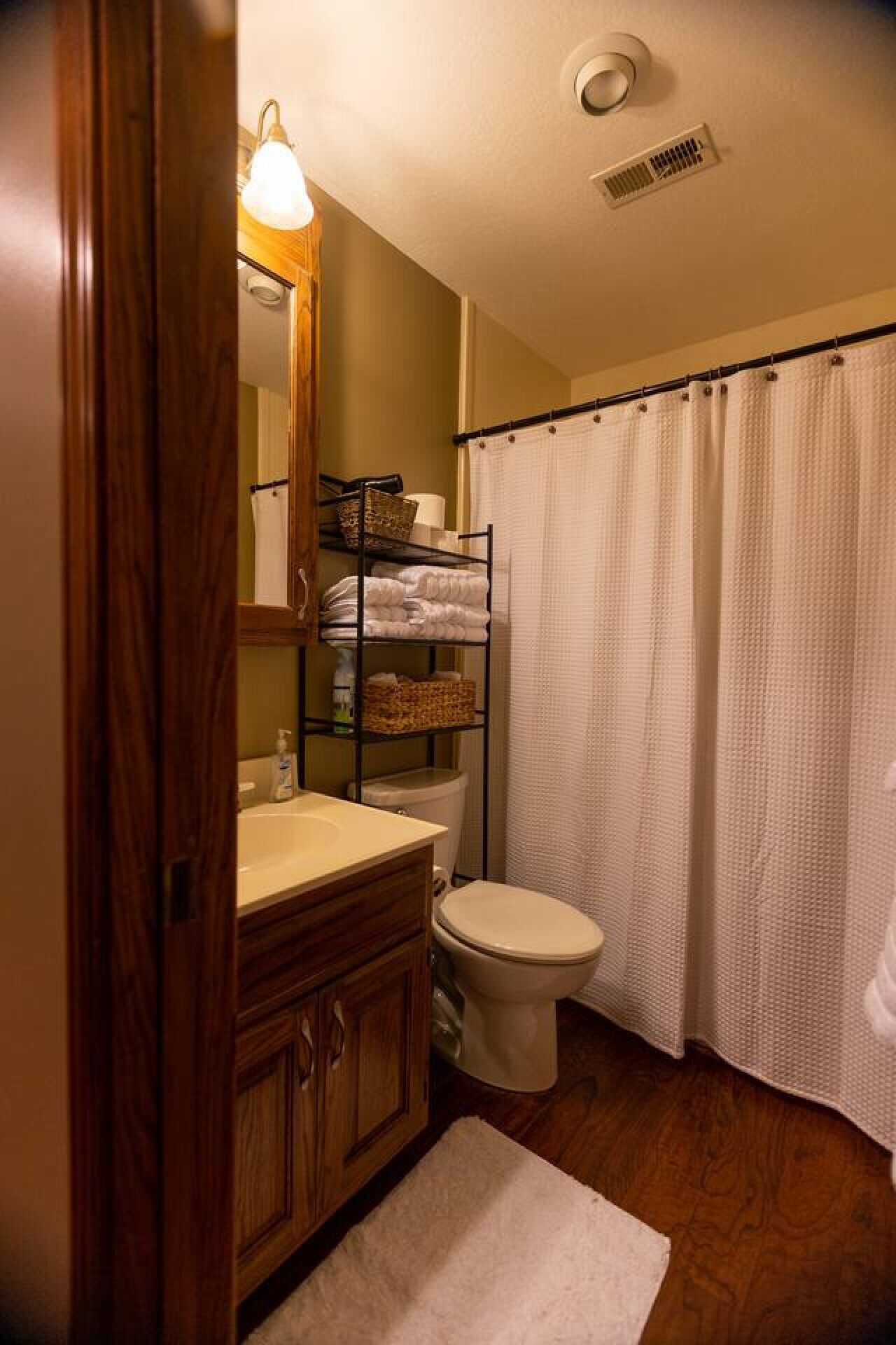 Une salle de bain avec un meuble-lavabo en bois, des toilettes, une étagère avec des serviettes et un rideau de douche.