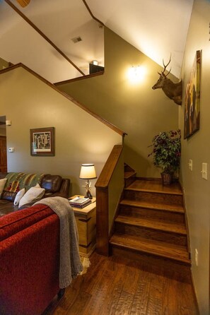 Eine Treppe mit Holzstufen, ein an der Wand befestigter Hirschschmuck, ein gerahmtes Bild, eine Lampe und ein Sofa mit Decke.