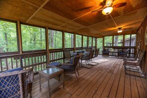 A covered outdoor area with wooden flooring, wicker furniture, and a ceiling fan.