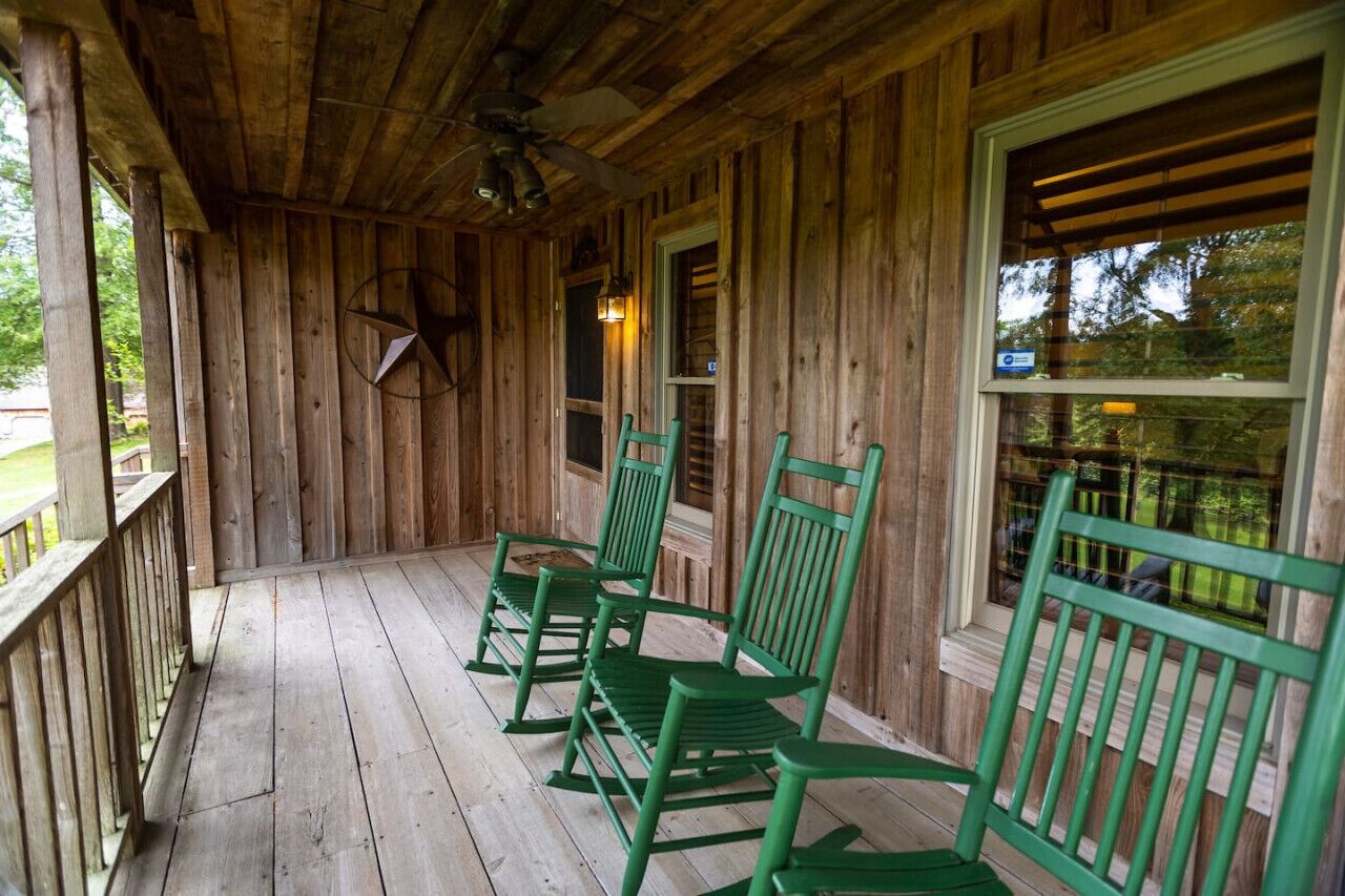 Une véranda en bois avec des fauteuils à bascule verts et un ventilateur de plafond.