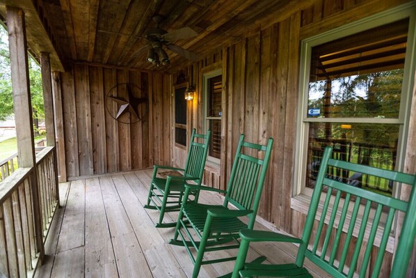 A wooden porch with green rocking chairs and a ceiling fan.