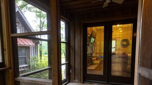A wooden porch with a ceiling fan, a view of a red-roofed building, and a glass door leading inside.