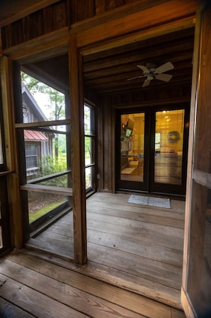 A wooden porch with a ceiling fan, a view of a red-roofed building, and a glass door leading inside.