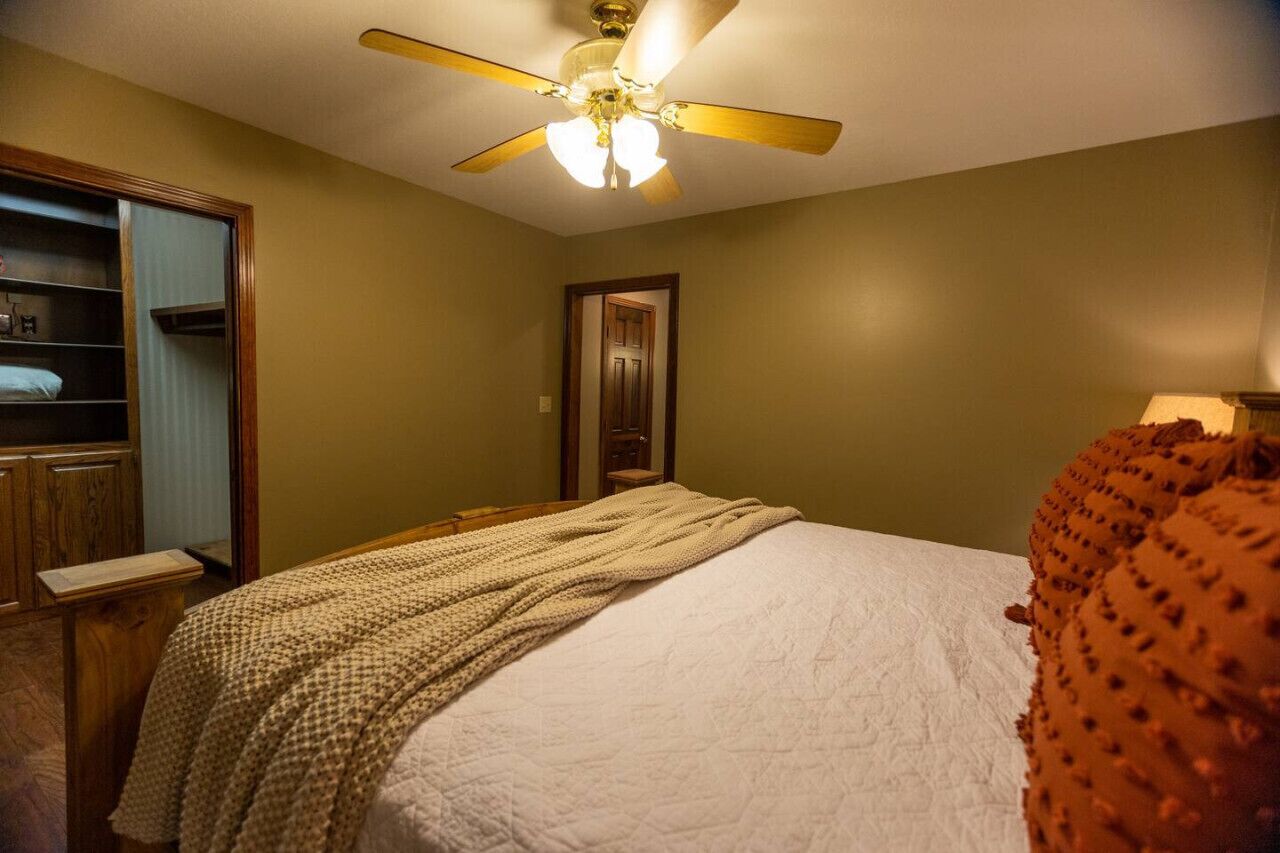 Une chambre à coucher avec un lit, un ventilateur de plafond, une armoire et une porte.