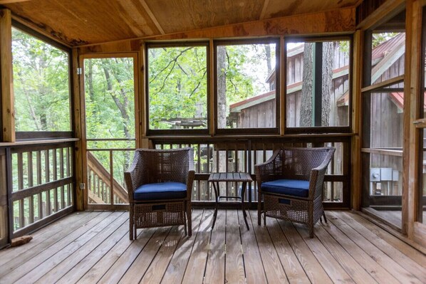 A wooden deck with wicker furniture and a table, overlooking a forested area.