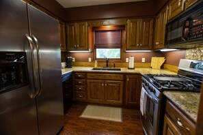A kitchen with wooden cabinets, a stainless steel refrigerator, a stove, and a window with blinds.