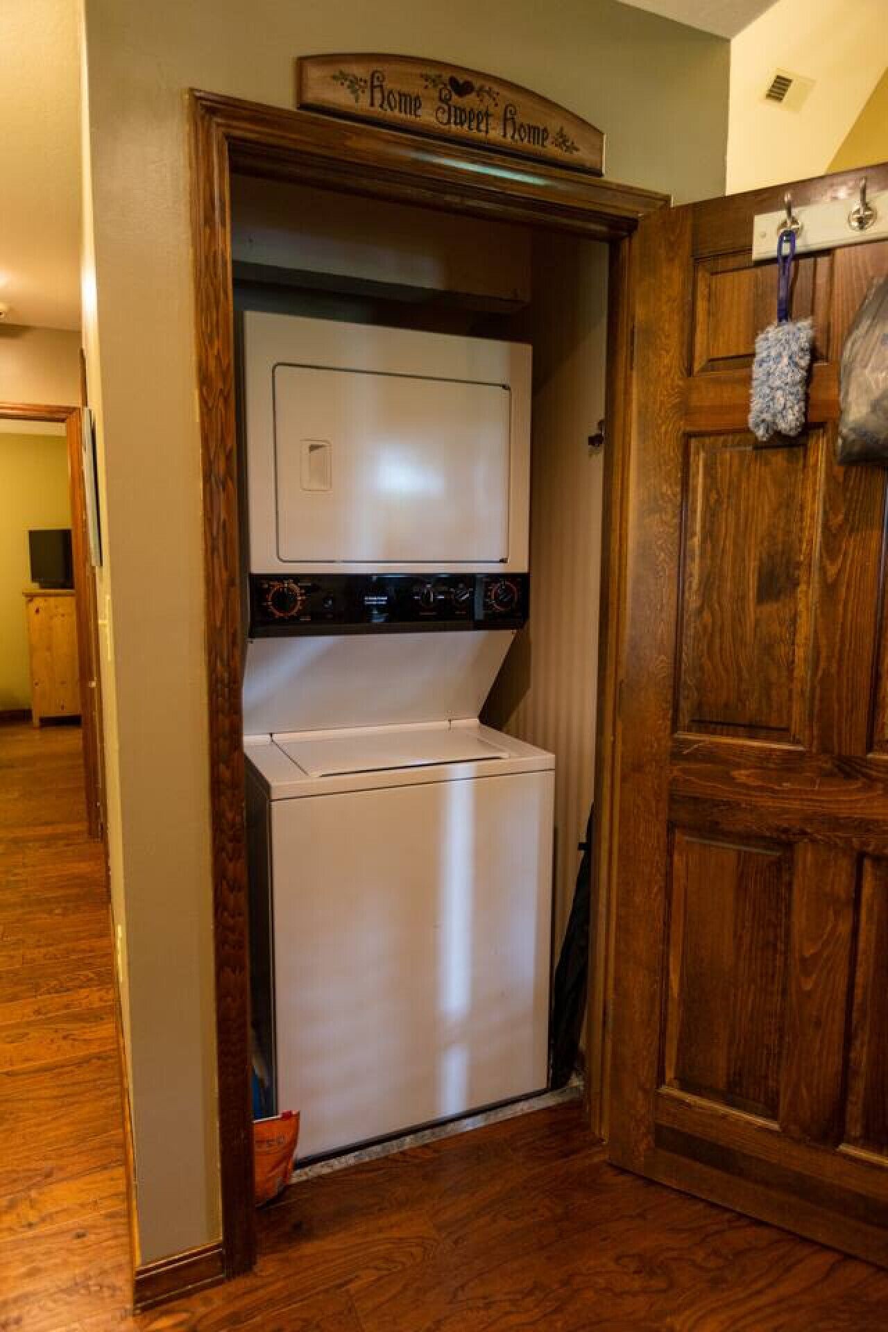 A laundry room with a washer and dryer, wooden flooring, and a sign above the door that reads "Home Sweet Home."