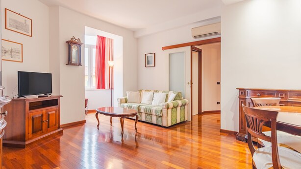 A living room with a television, a sofa, a dining table, and a wooden cabinet. - Residenza Edvige - Italian Homing (Verona)