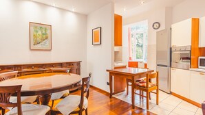 A dining area with a wooden table and chairs, a kitchen with white cabinets and appliances, and a window with a view of greenery. - Residenza Edvige - Italian Homing (Verona)