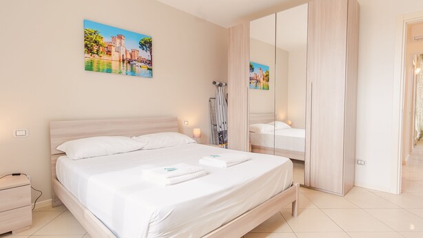 A modern hotel room with a large bed, a bedside table, a mirror, and artwork on the walls. - Galleria Il Principe - Italian Homing (Desenzano del Garda)