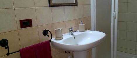 Un baño con un lavamanos blanco, un espejo y una toalla roja colgada en un perchero.
