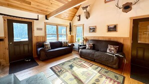 A cozy cabin interior with wooden ceilings, two sofas, a rug, and deer antlers on the wall. - Caddis Ridge Camp|West Forks with Trail Access (West Forks)