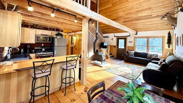 A wooden interior with a kitchen, bar area, and seating. - Caddis Ridge Camp|West Forks with Trail Access (West Forks)