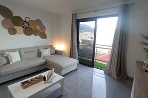 Una sala de estar moderna con un sofá modular, una mesa de centro y vistas a un paisaje urbano a través de un amplio ventanal corredero.